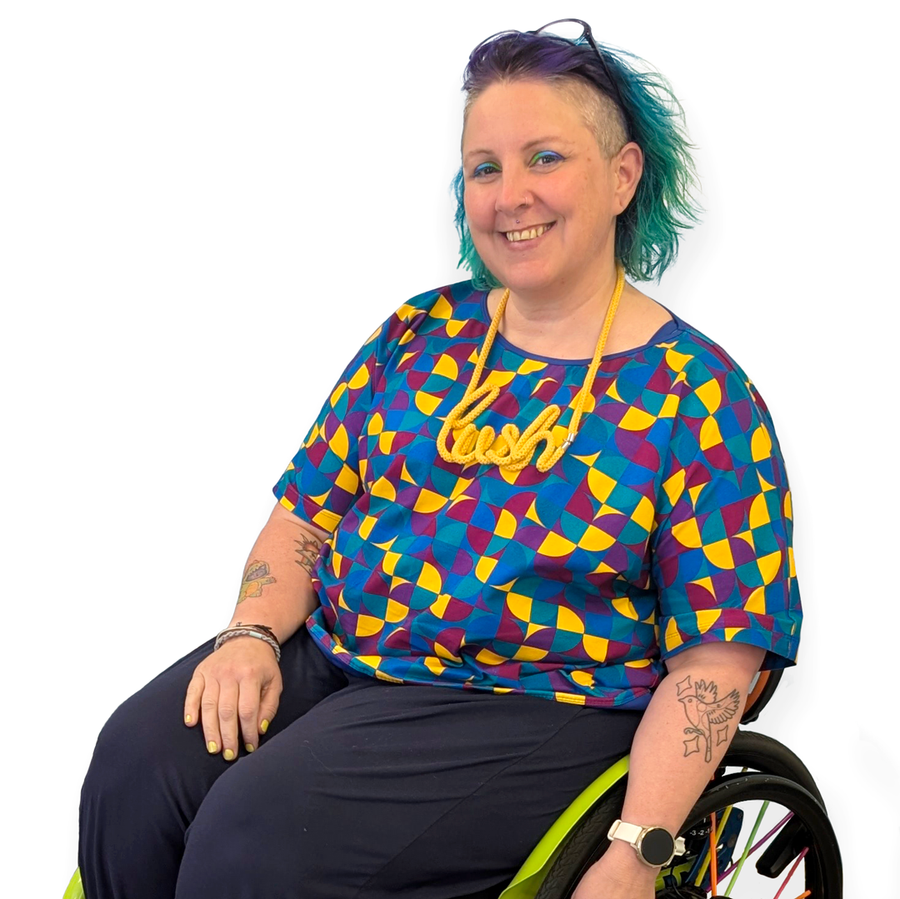 Kirsty sitting in their wheelchair wearing a boxy cotton t-shirt in a busy geometric pattern.
